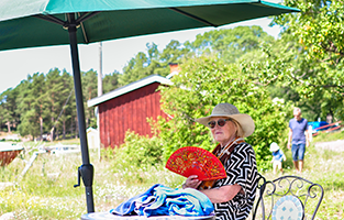 Äldre kvinna sitter ute under ett parasoll en solig sommardag.
