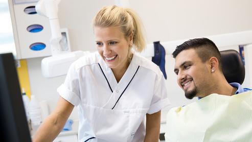 Tandvårdspersonal och patient tittar tillsammans på en datorskärm