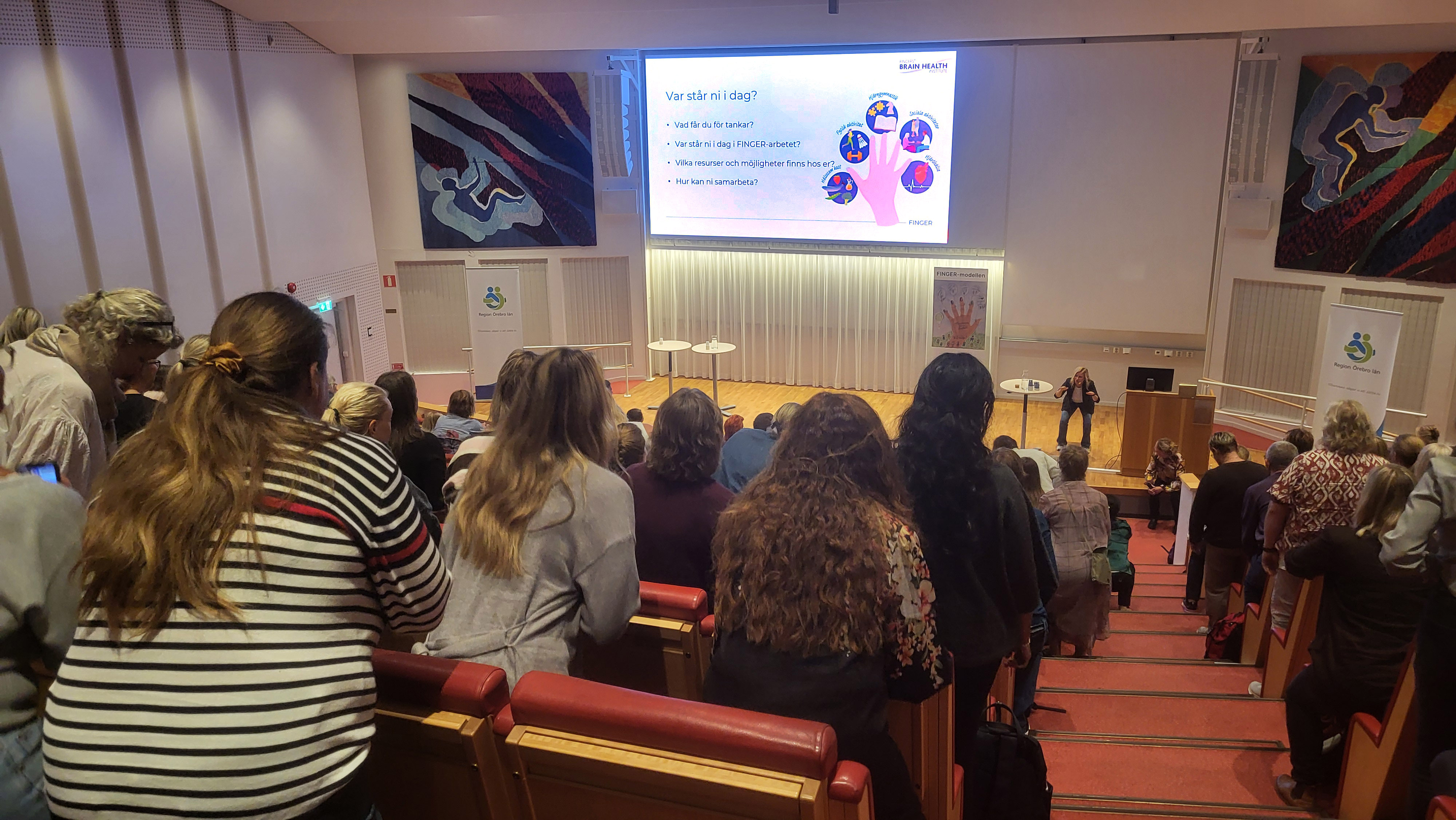 Hela publiken gör benböj medan föreläsaren talar om "Var står vi?"