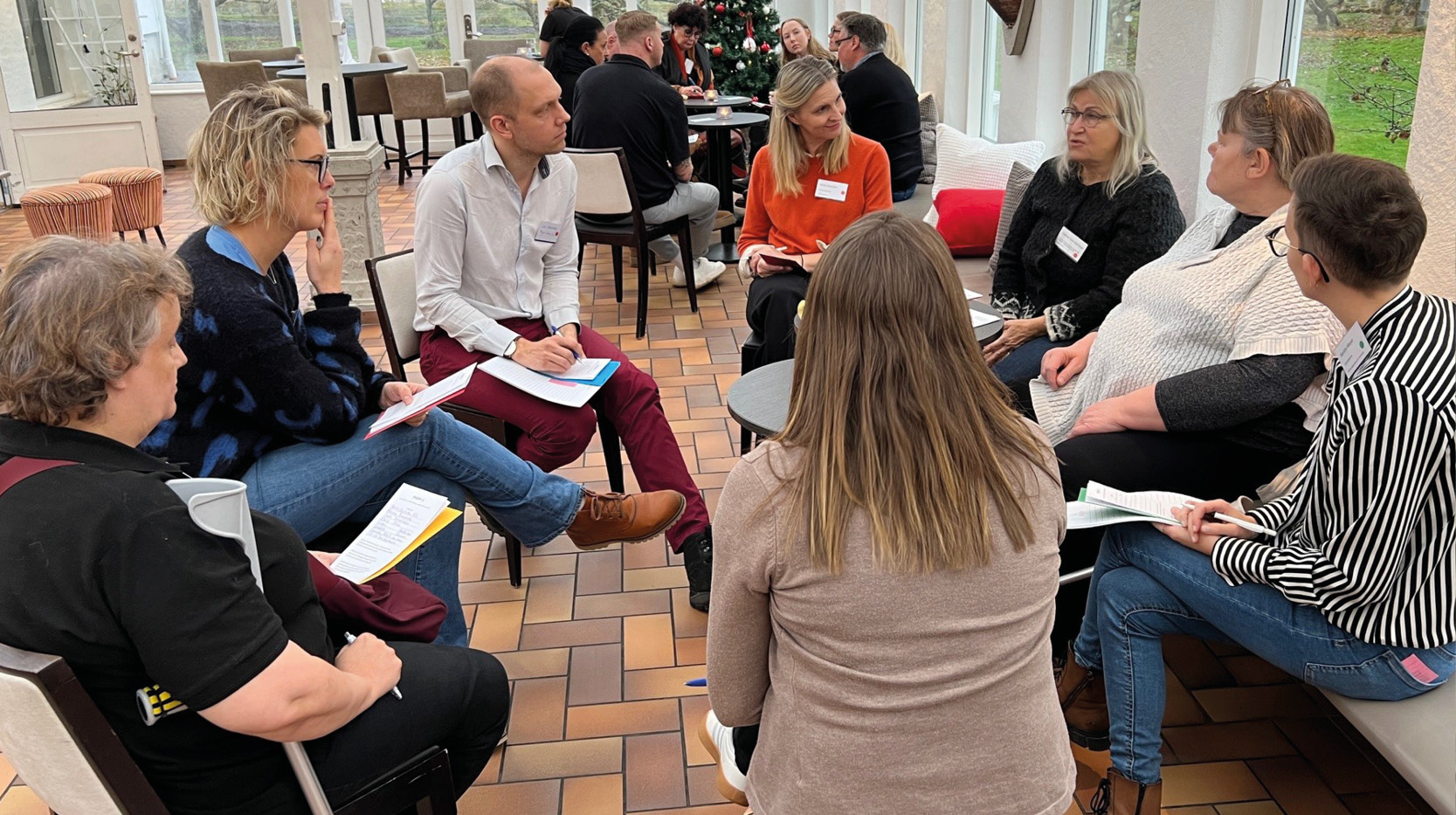 Åtta workshopdeltagare sitter i en cirkel  och samtalar i ett orangeri